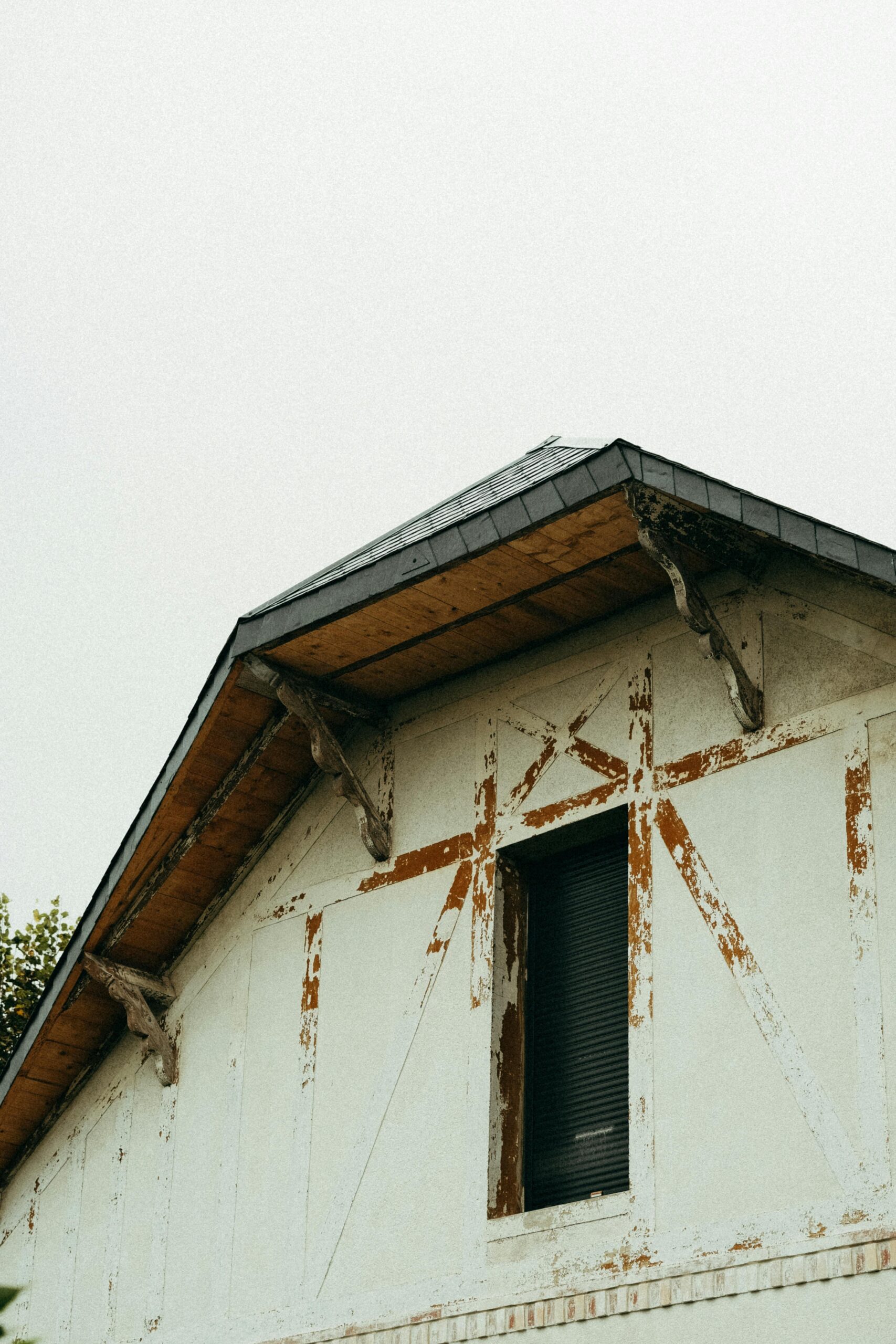 Close-up of a rustic, weathered house with gabled roof, showing peeling paint and vintage architecture.