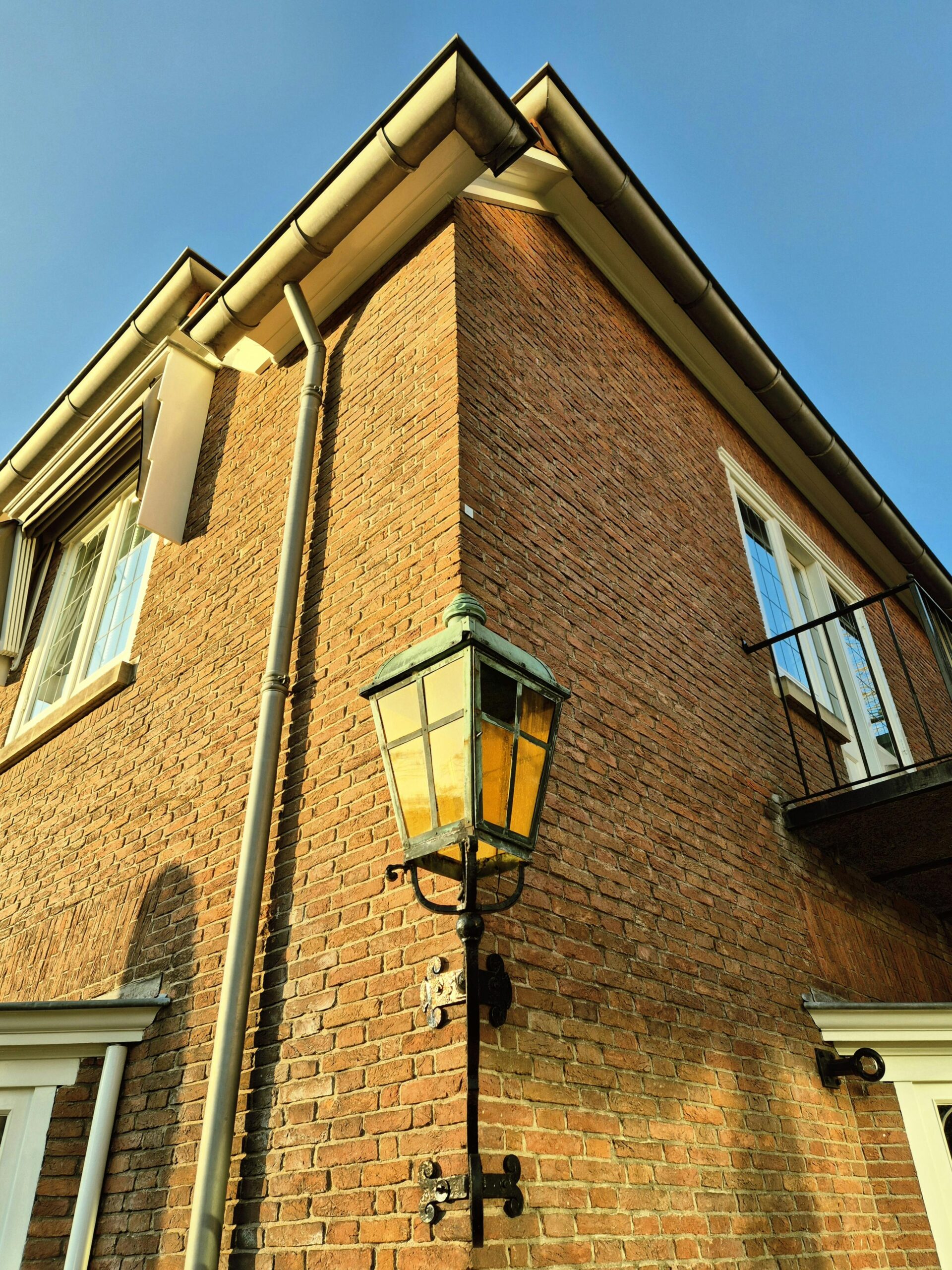 Corner view of a brick house with a vintage lantern under clear skies.
