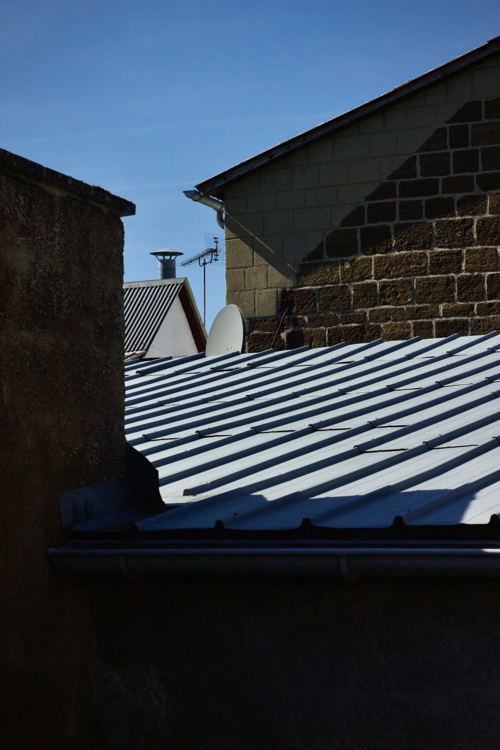 Abstract view of urban rooftops with dramatic shadow patterns under clear sky.