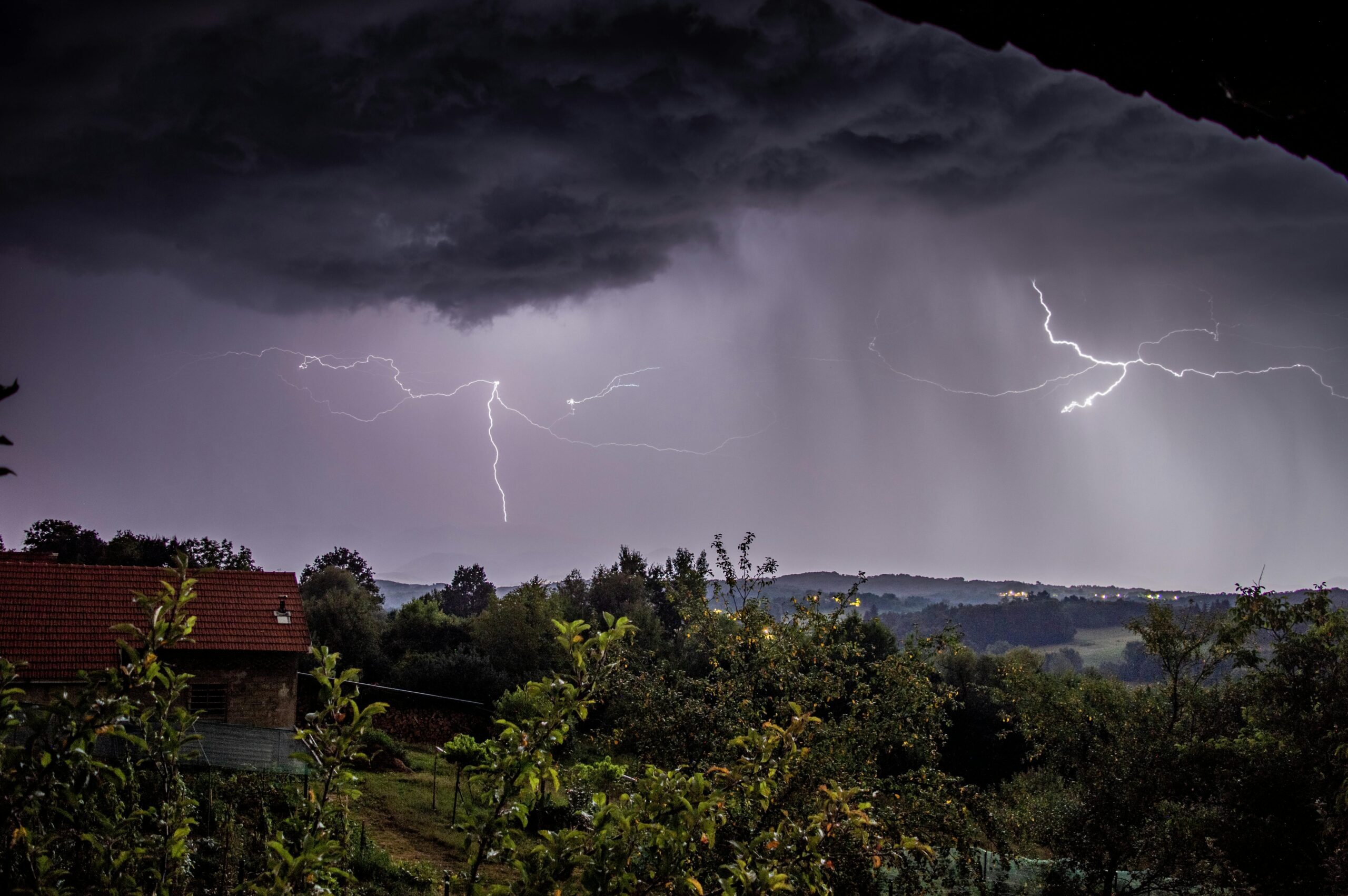 A dramatic thunderstorm illuminates the countryside with striking lightning over a rural landscape.