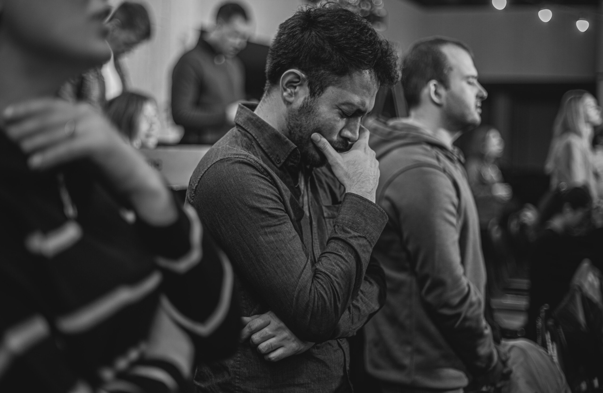 Black and white photo of a man deep in thought in a social gathering.